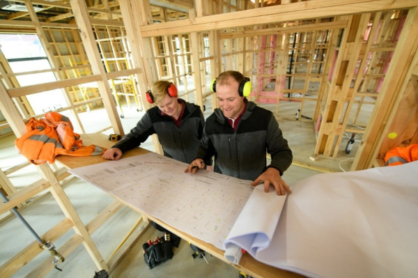 Two people on a building site checking plans for a large timber construction project