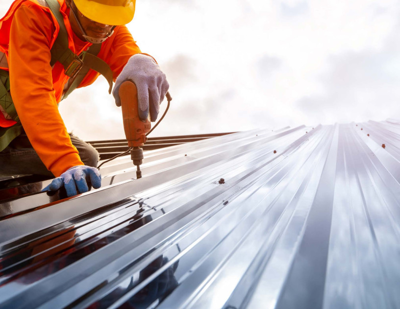 A person with safety gear on drilling a hole on the roof